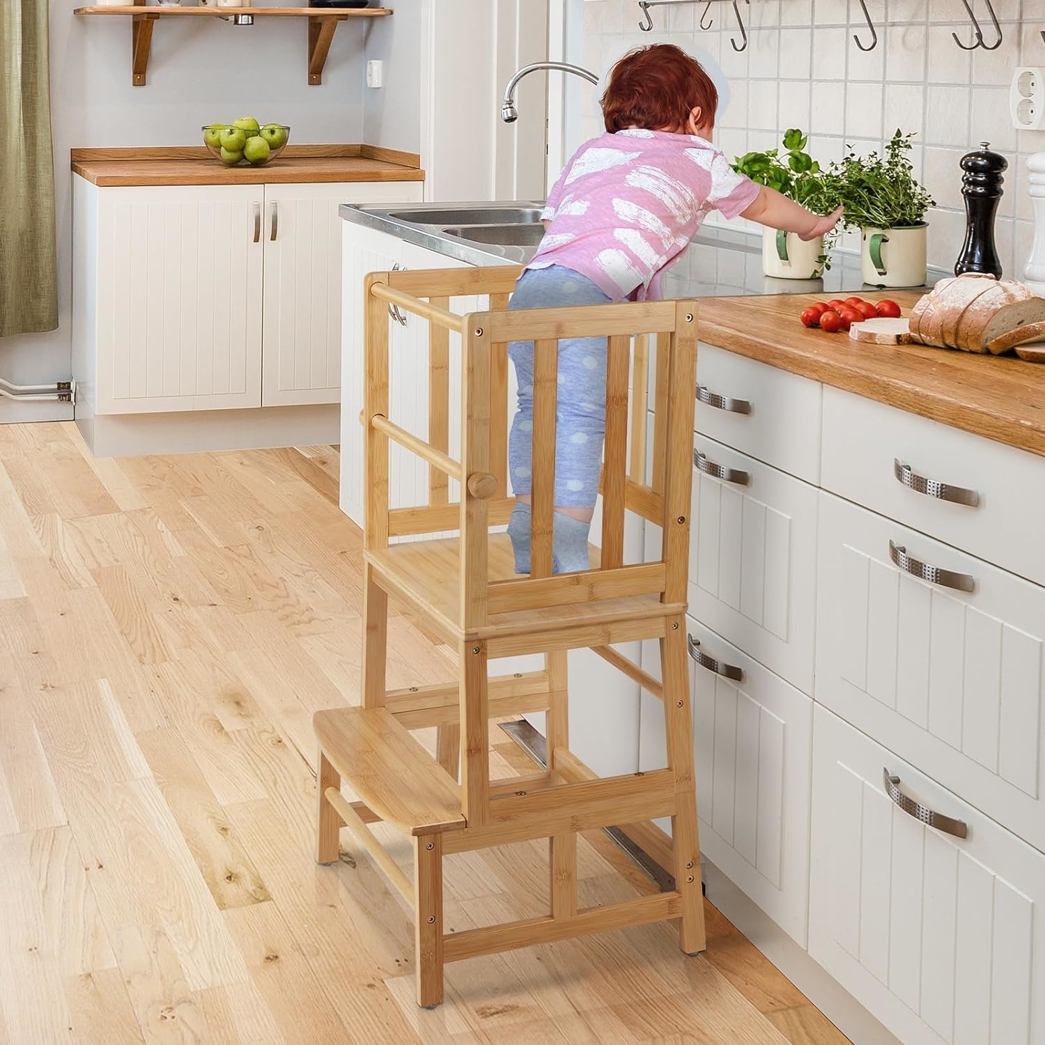 Child stands on a wooden learning tower in a kitchen, reaching the countertop safely