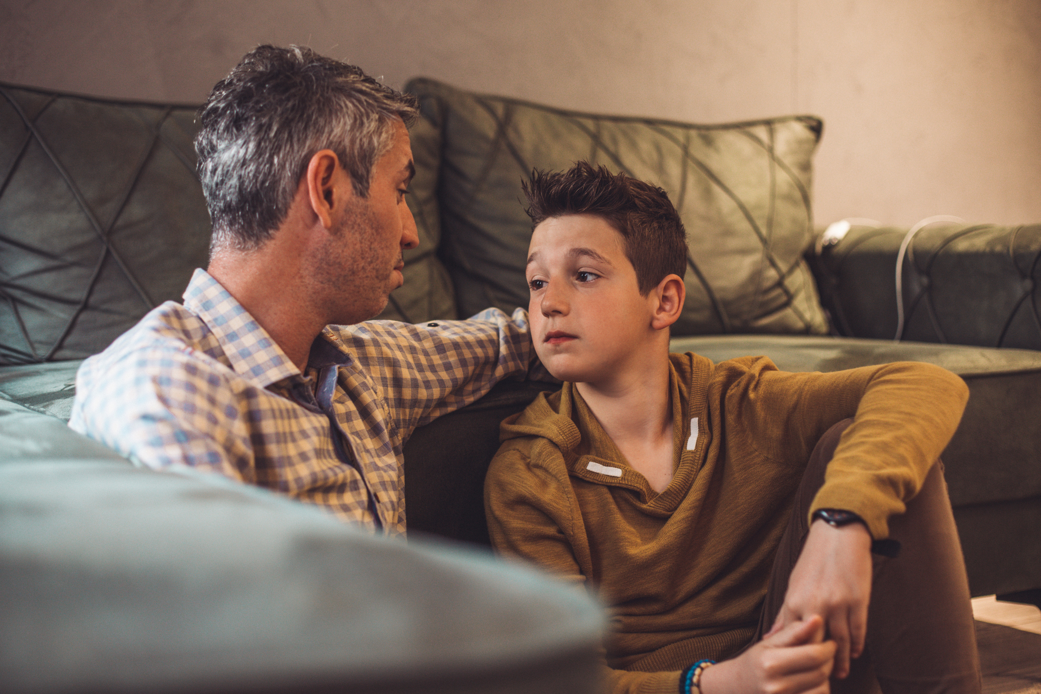 Man and boy sitting on couch in a serious conversation, reflecting a parenting moment