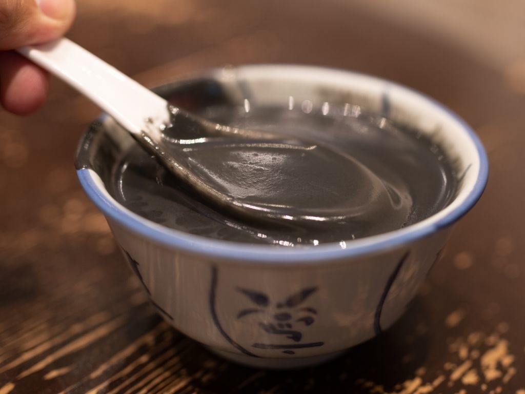 A bowl of thick, dark soup with a spoon partially submerged, on a wooden surface
