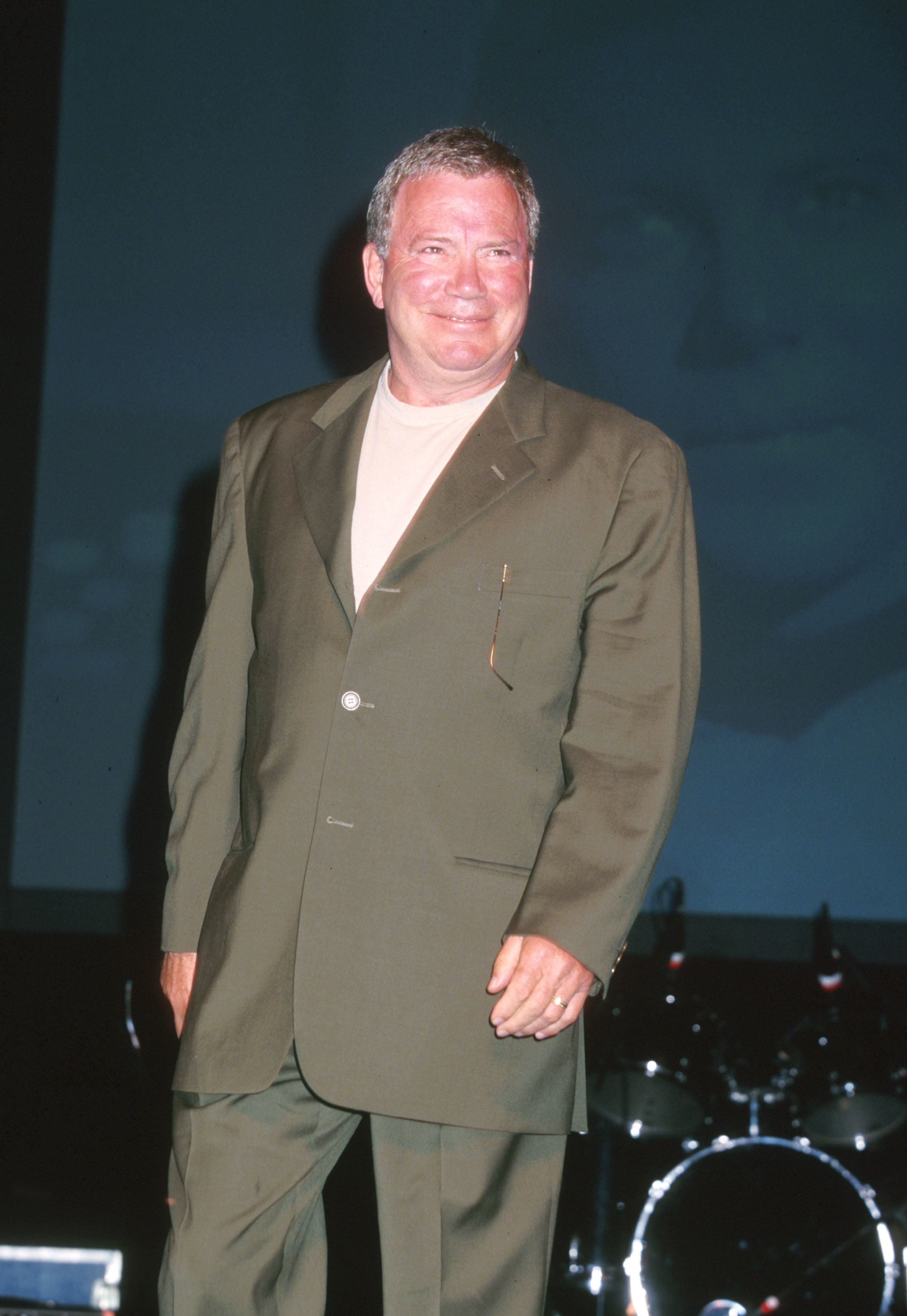 Man smiling in a formal olive suit poses for a photo at an event