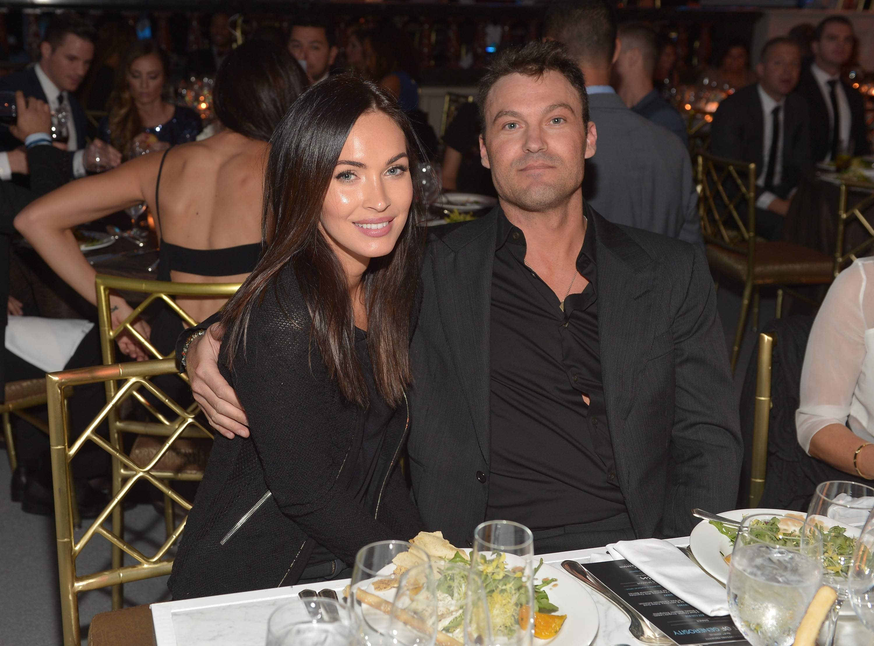 Megan Fox and Brian Austin Green sitting together at an event with dinner plates in front of them