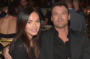 Megan Fox in a black outfit and Brian Austin Green in a black suit sitting together at an event