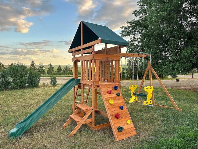 Wooden playset with slide, swings, and climbing wall in an outdoor setting. Suitable for children's backyard play