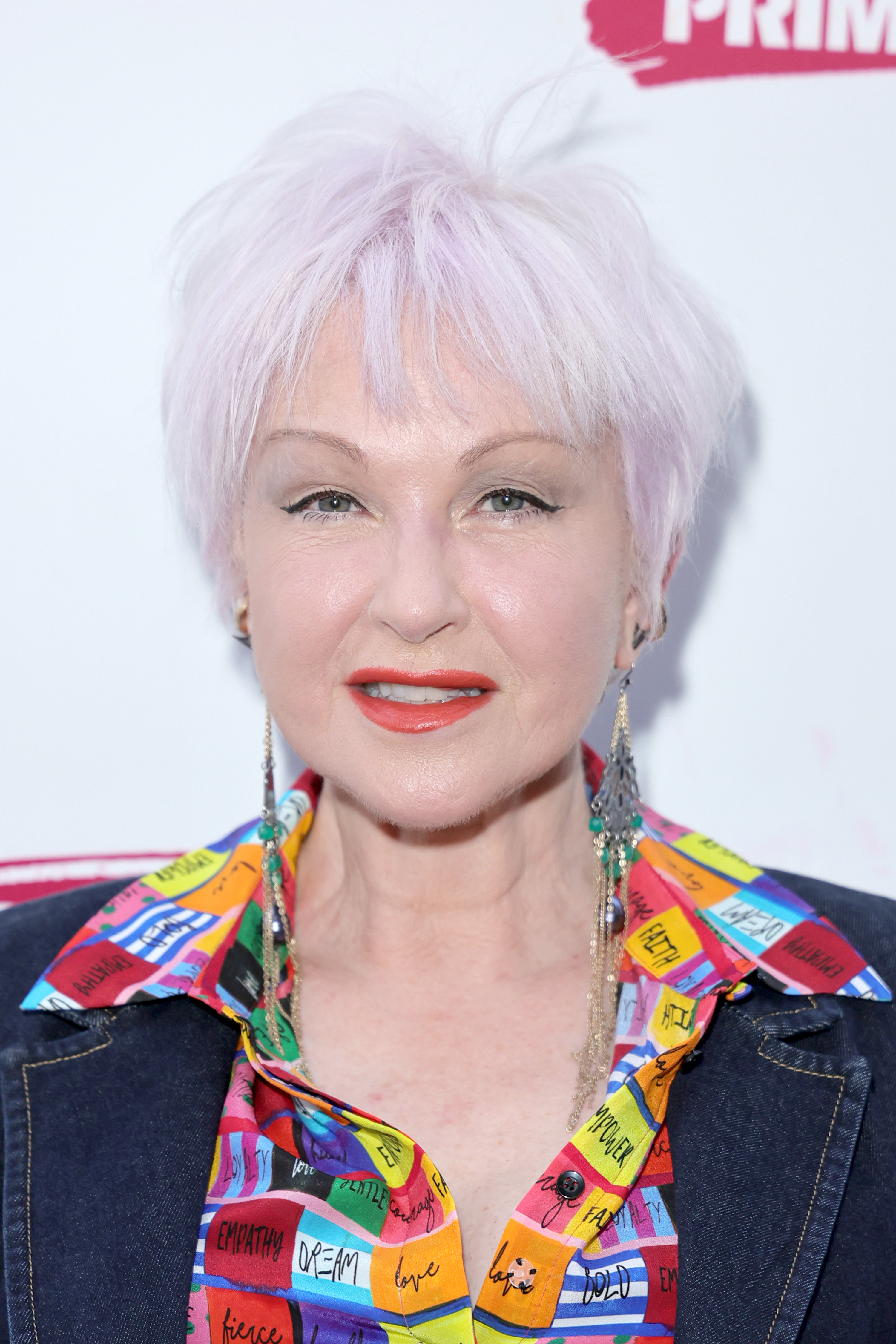 Cyndi Lauper with short hair wearing a colorful blouse and denim jacket
