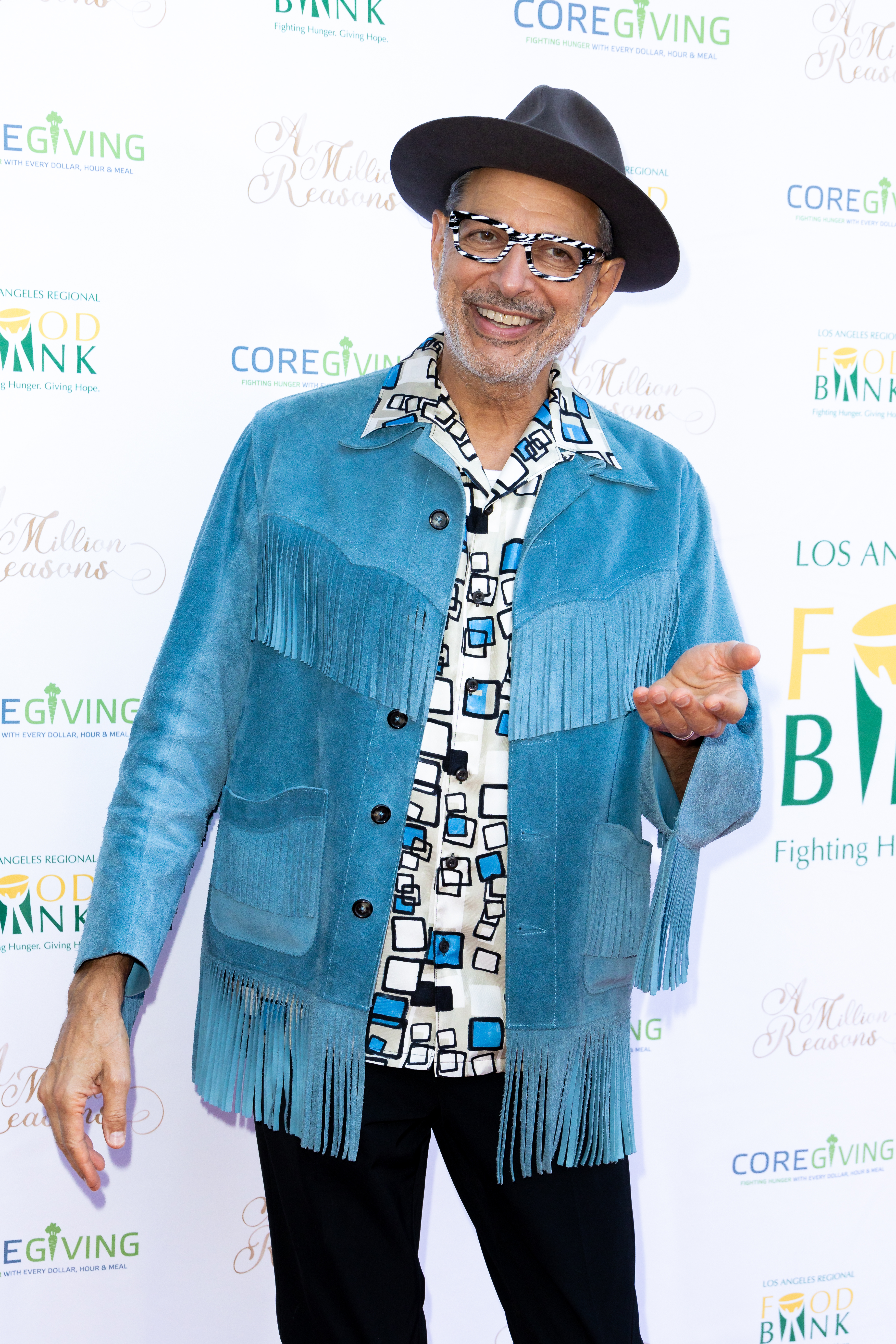 Man in a fringed blue jacket and hat smiling at a charity event