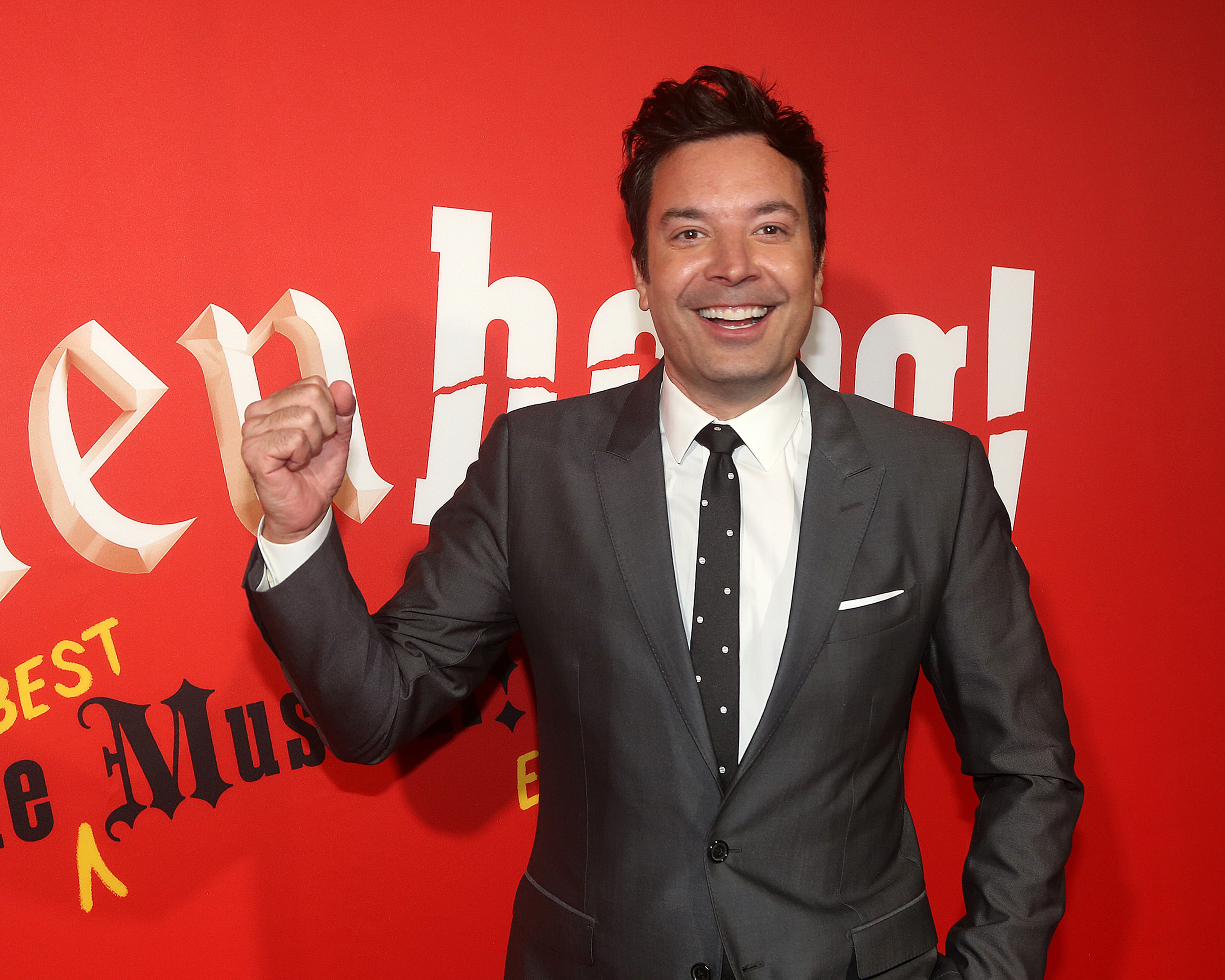 jimmy in a suit with a polka dot tie posing with a raised fist in front of a promotional backdrop
