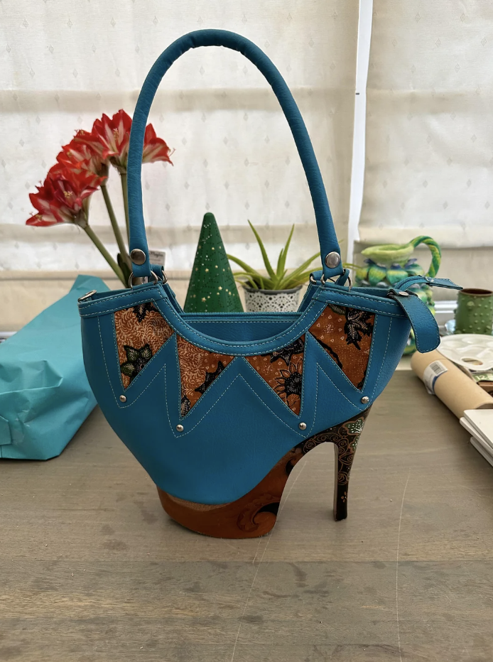 A unique high-heel shoe fashioned into a handbag with decorative patterns stands on a table