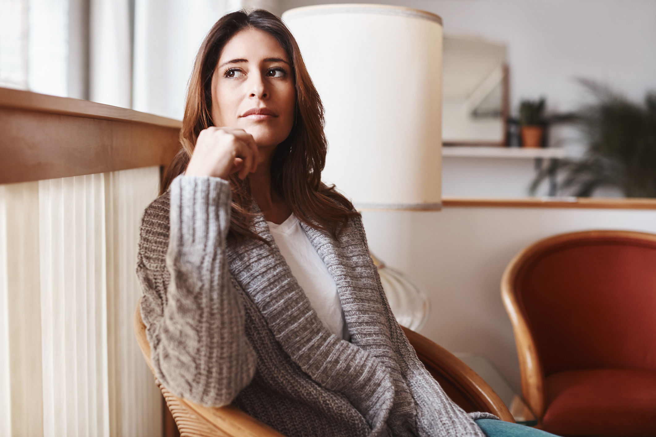 Woman in a sweater sitting thoughtfully in a chair, looking away
