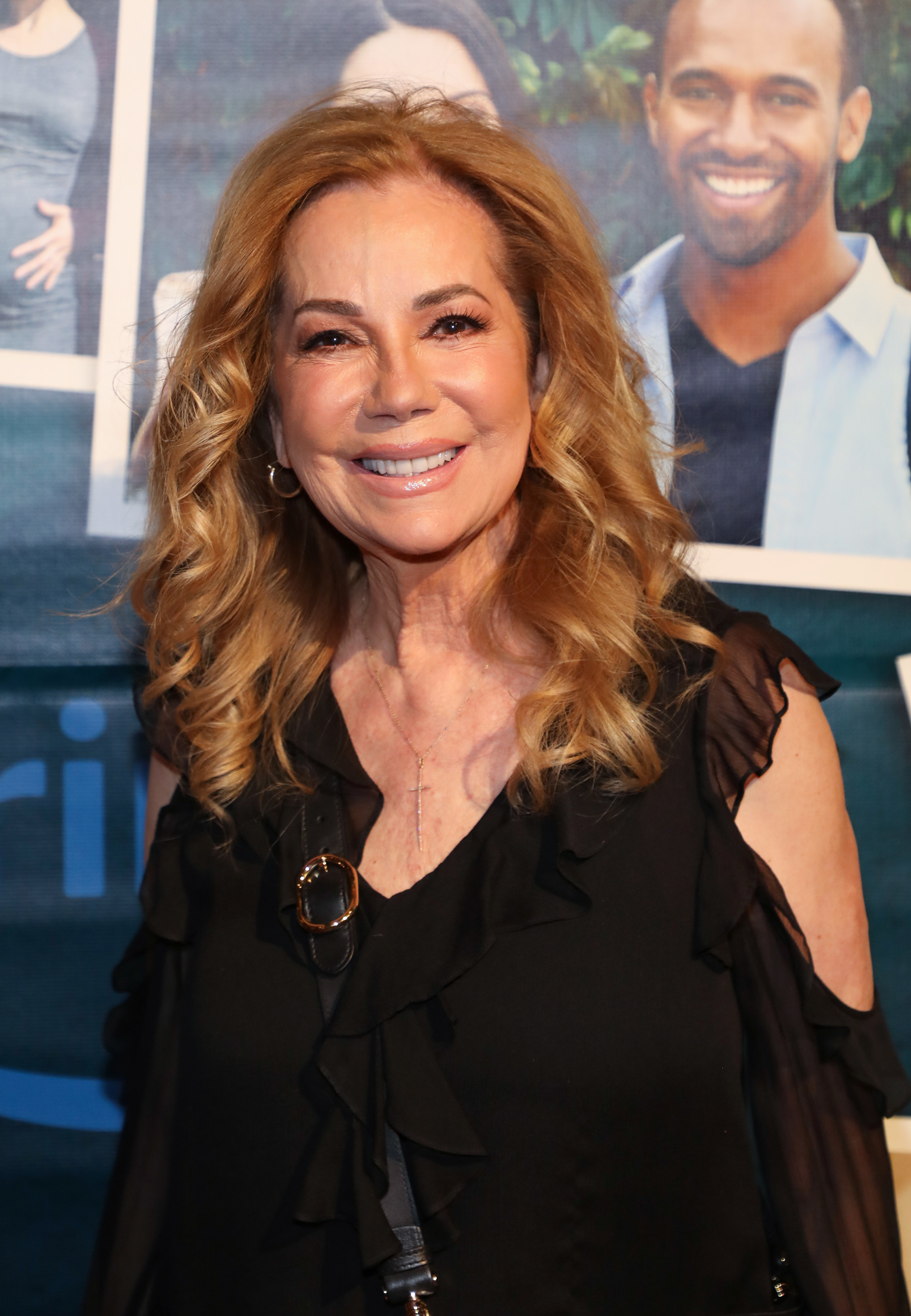 Woman in a ruffled black dress smiling at an event, with movie posters in the background