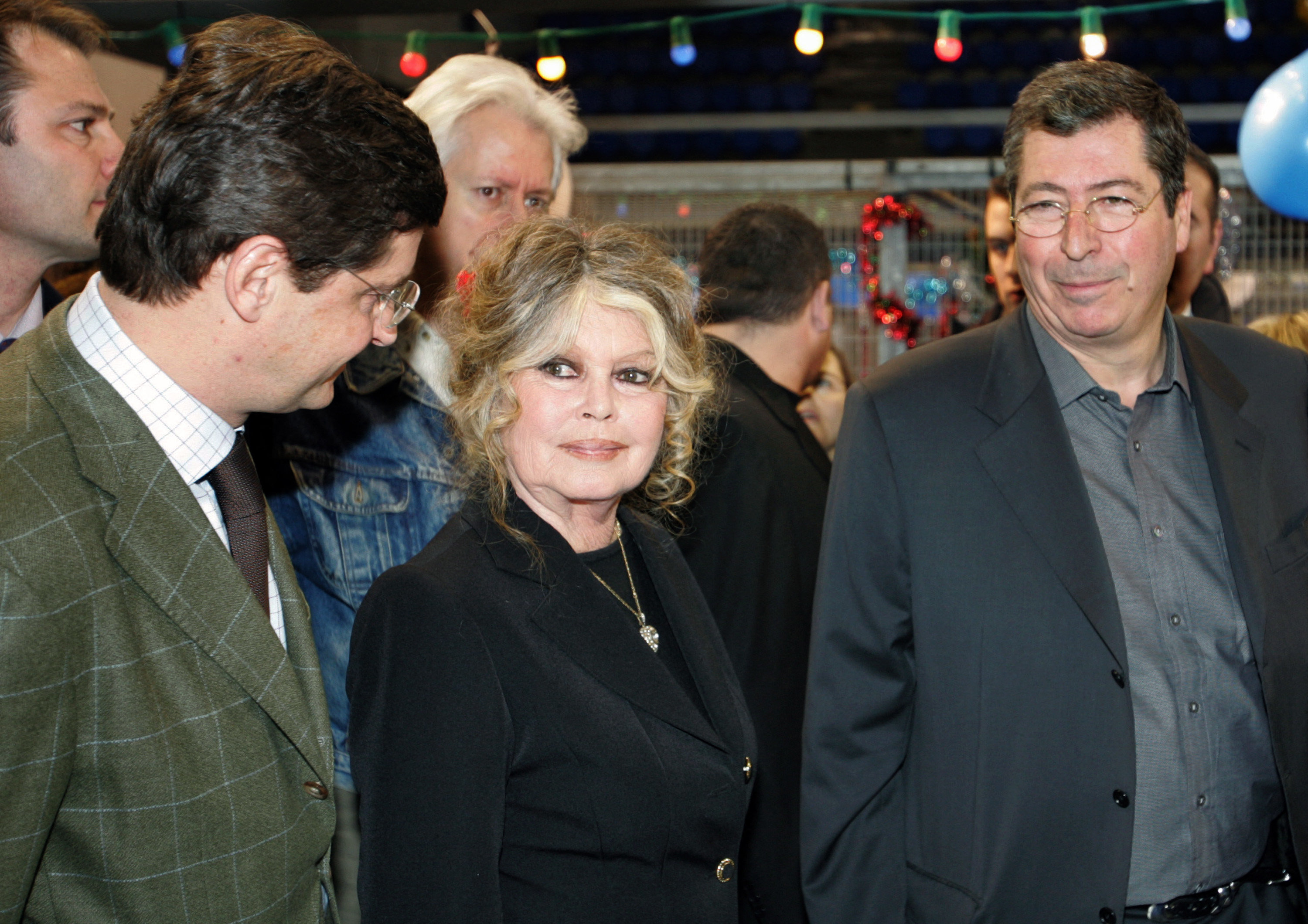 Three individuals at an event, middle person wearing a dark jacket and scarf