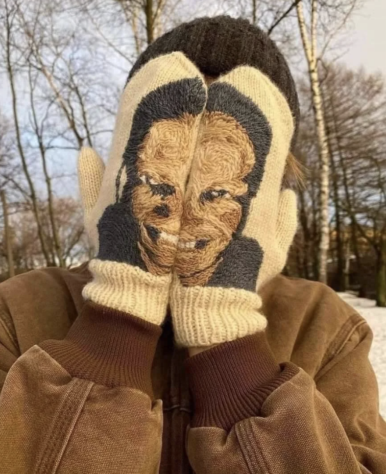 Person holding a pair of gloves with a face knit into the design in front of their face