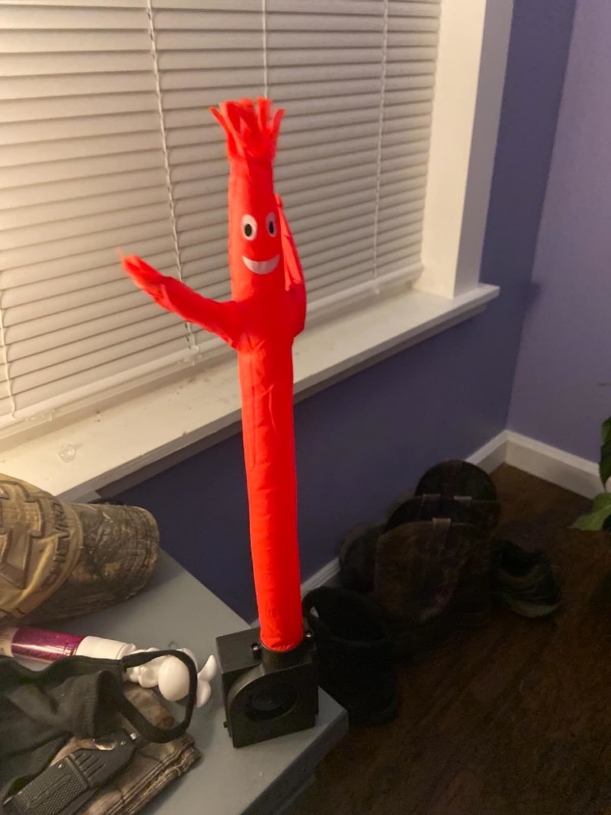 Inflatable tube man decoration indoors next to a window and various items on the floor