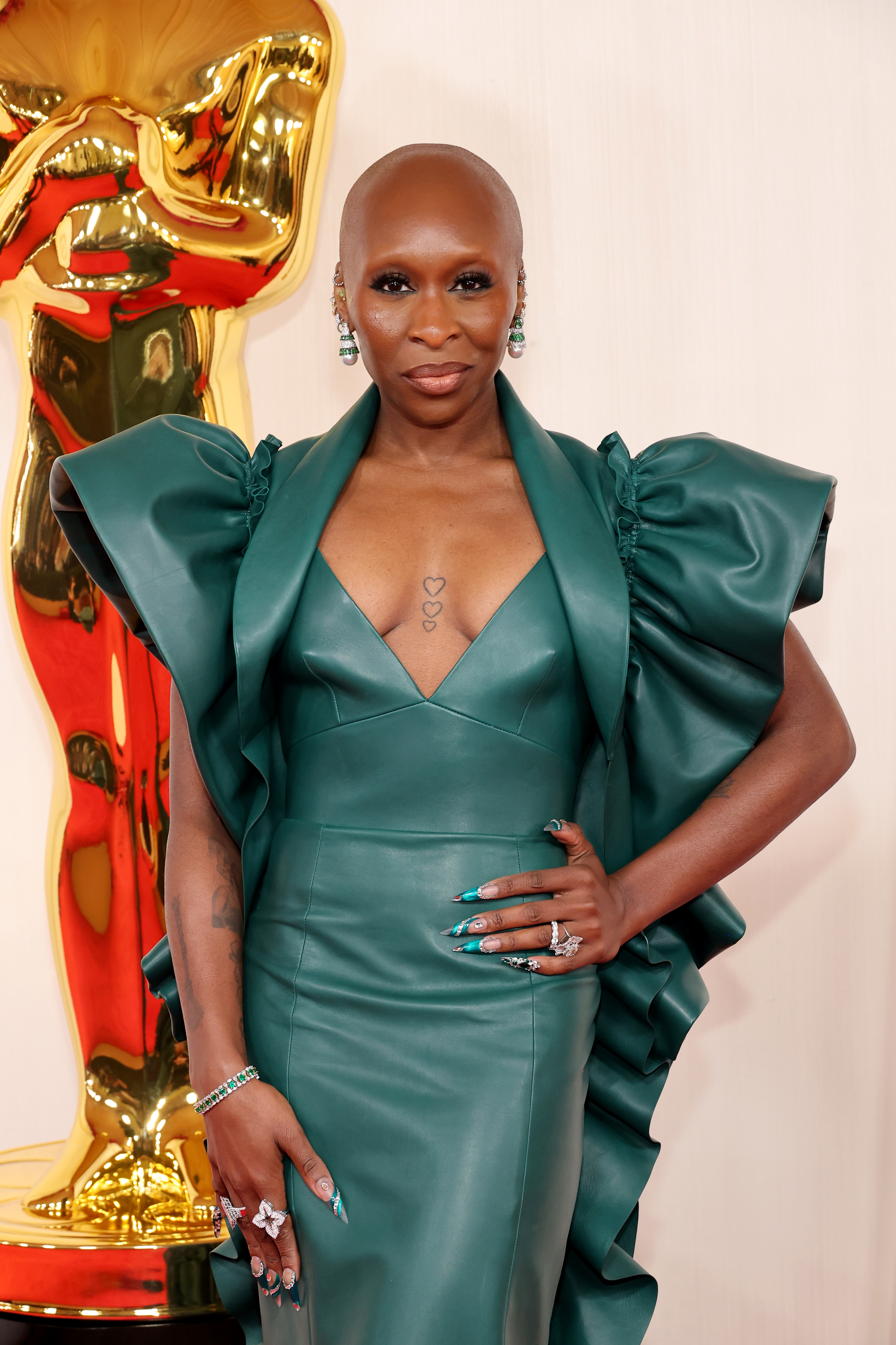 Cynthia posing at an event in an elegant green dress with prominent shoulder detailing and a plunging neckline