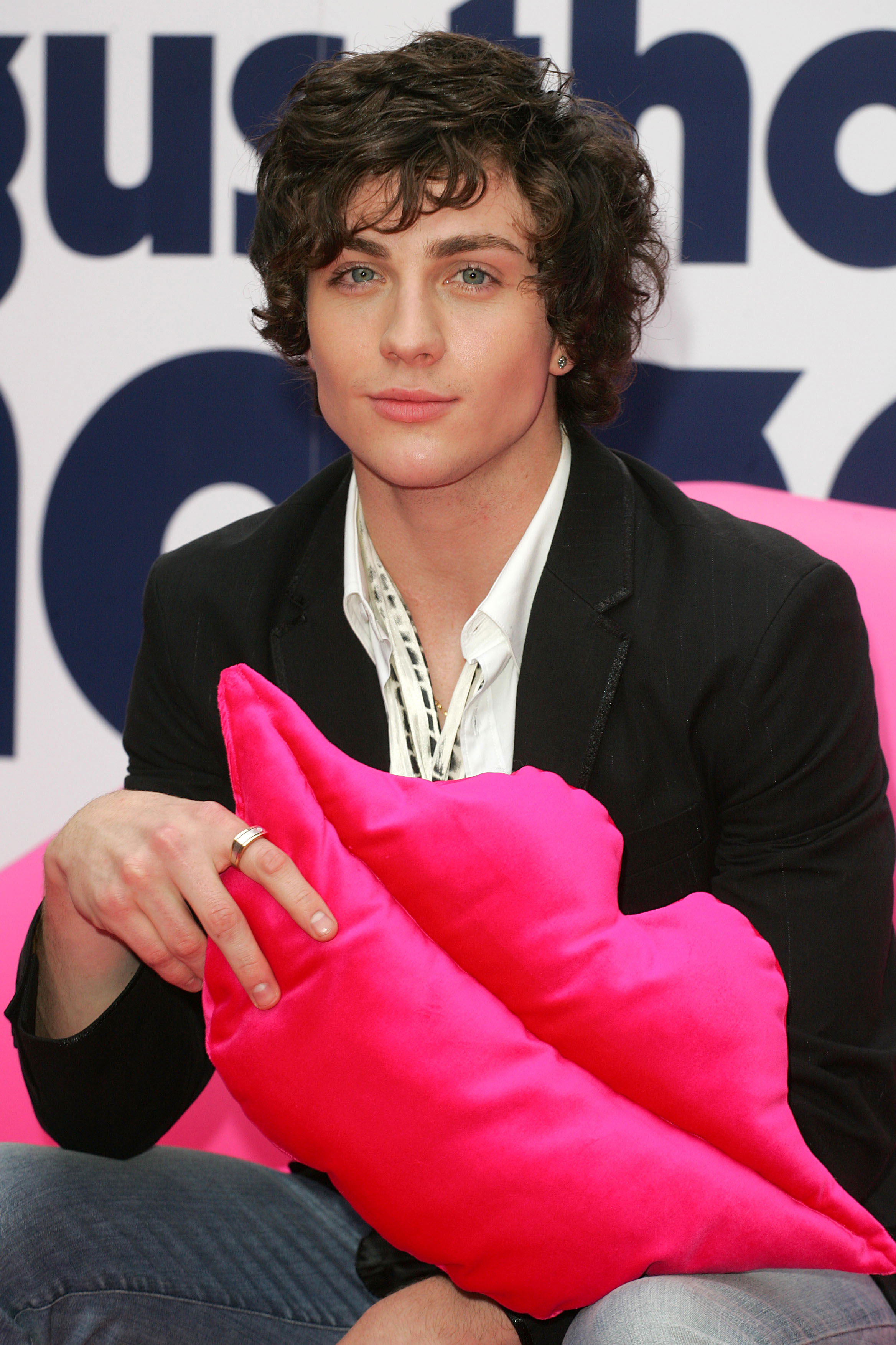 A closeup of a much younger Aaron Taylor-Johnson holding a plushie of a pair of lips at an event