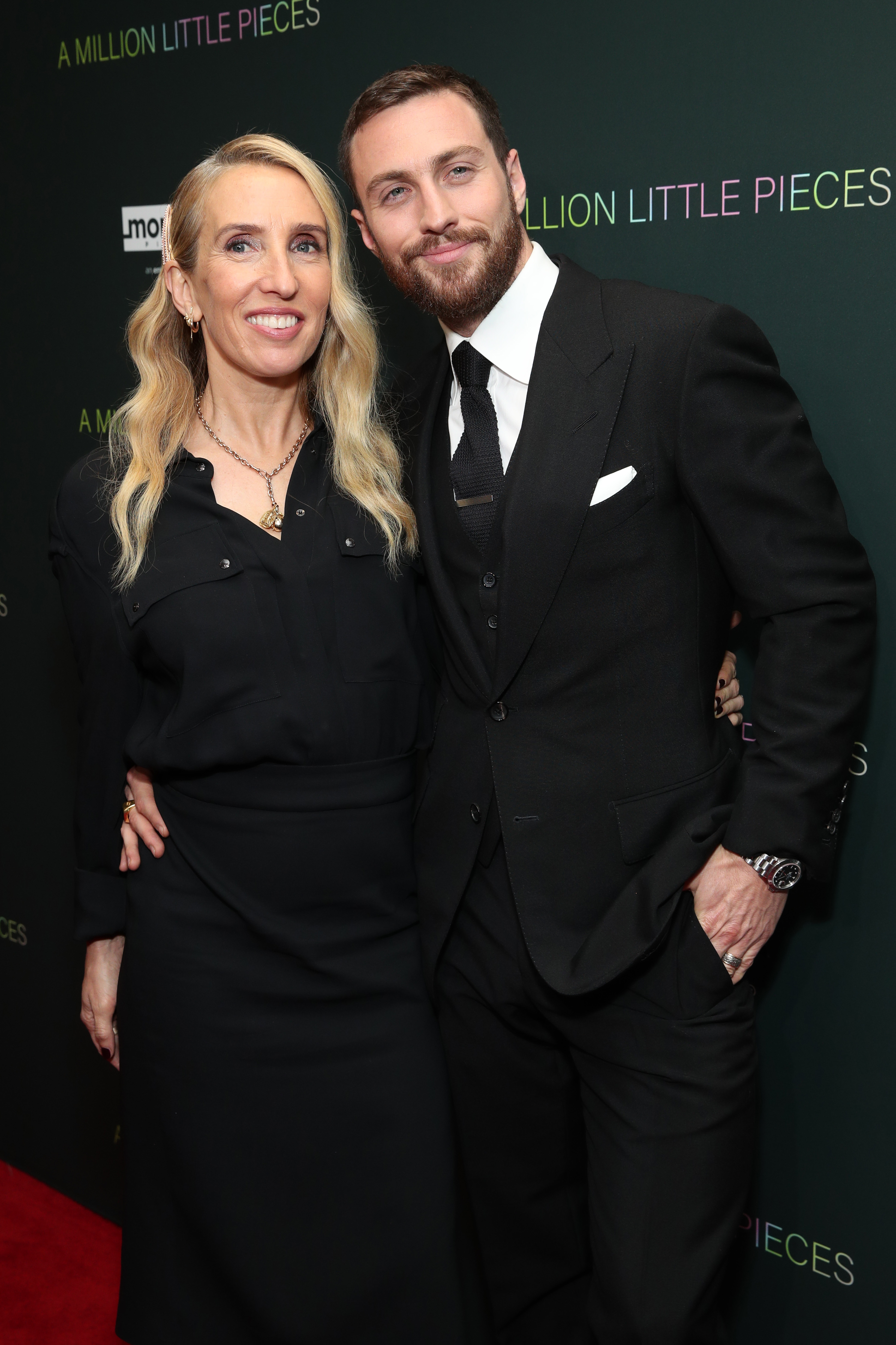 Sam Taylor-Johnson and Aaron Taylor-Johnson posing together; Sam in a dress and Aaron in a suit