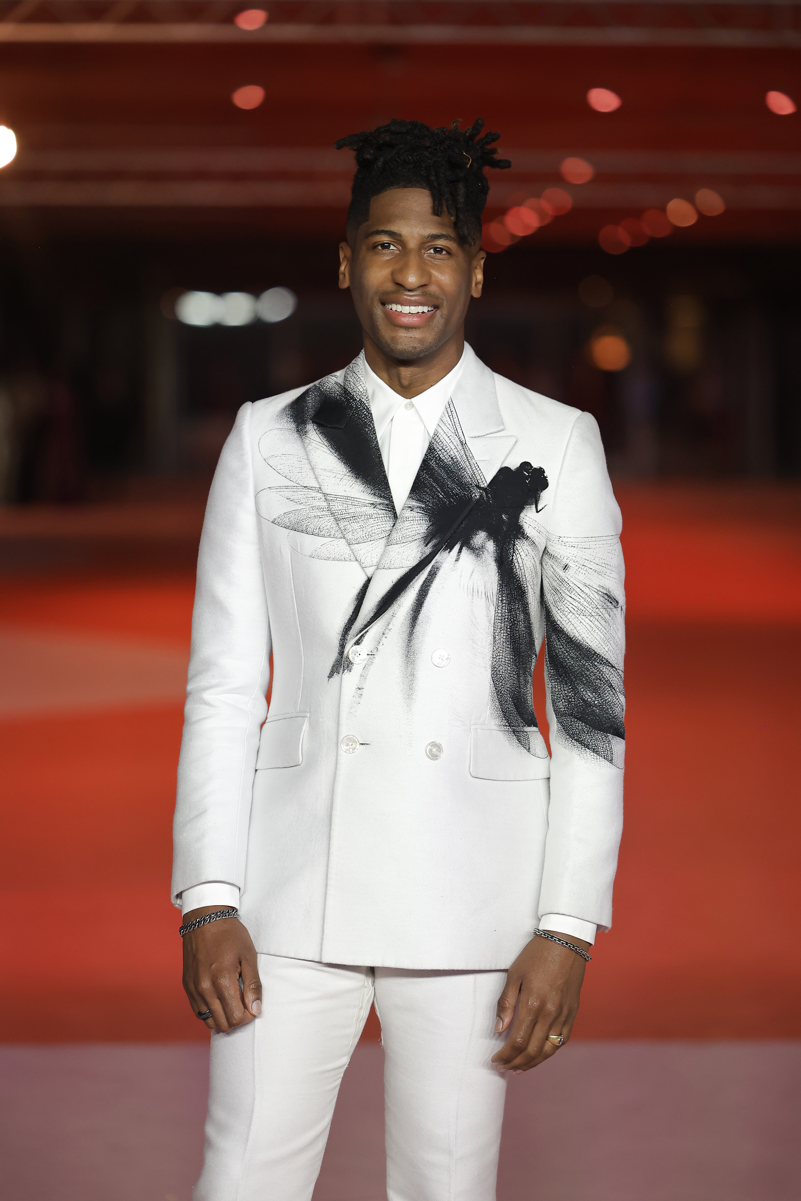 Person in a white jacket with a black and white graphic design and bow detail, standing on the red carpet