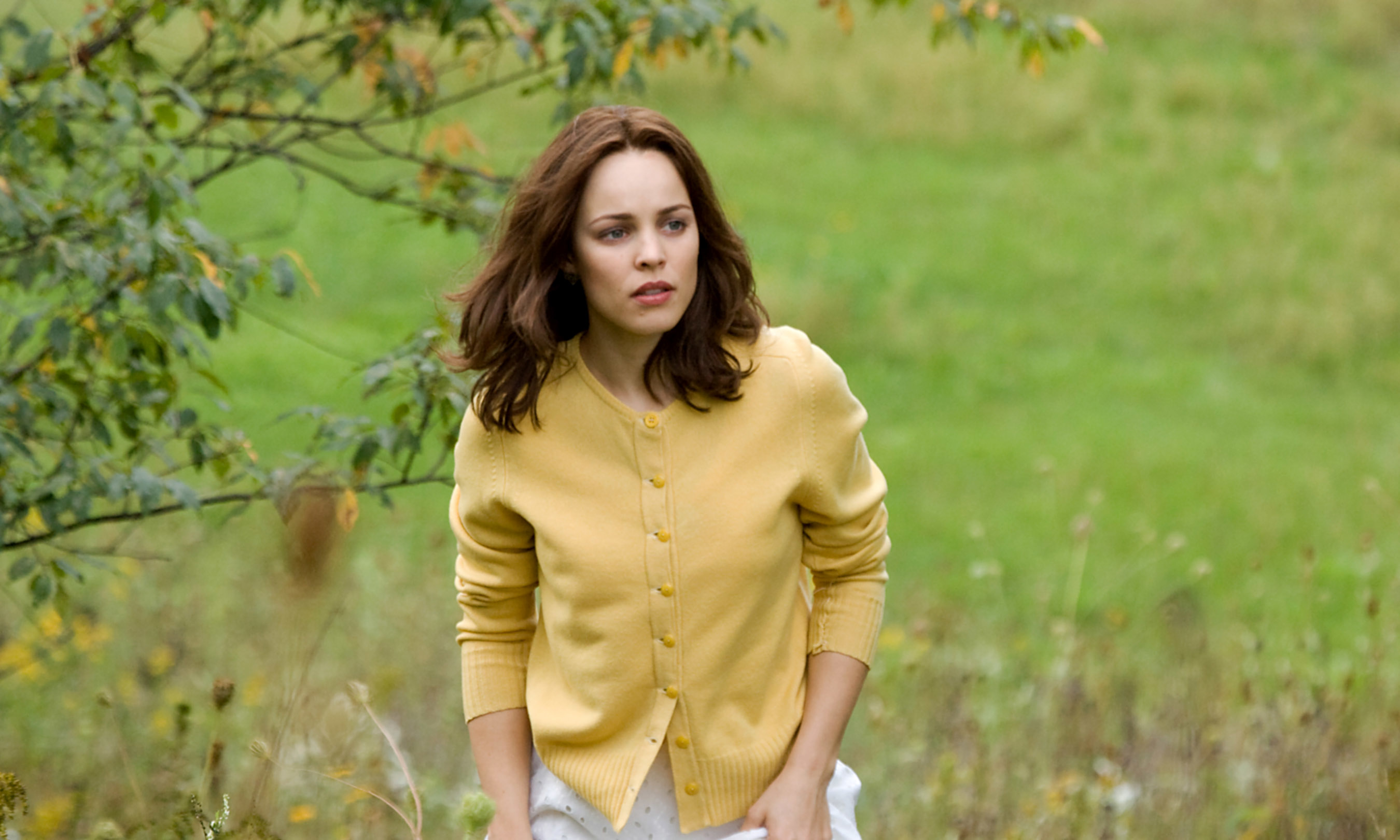 Clare wearing a cardigan and skirt, looking pensive in a field