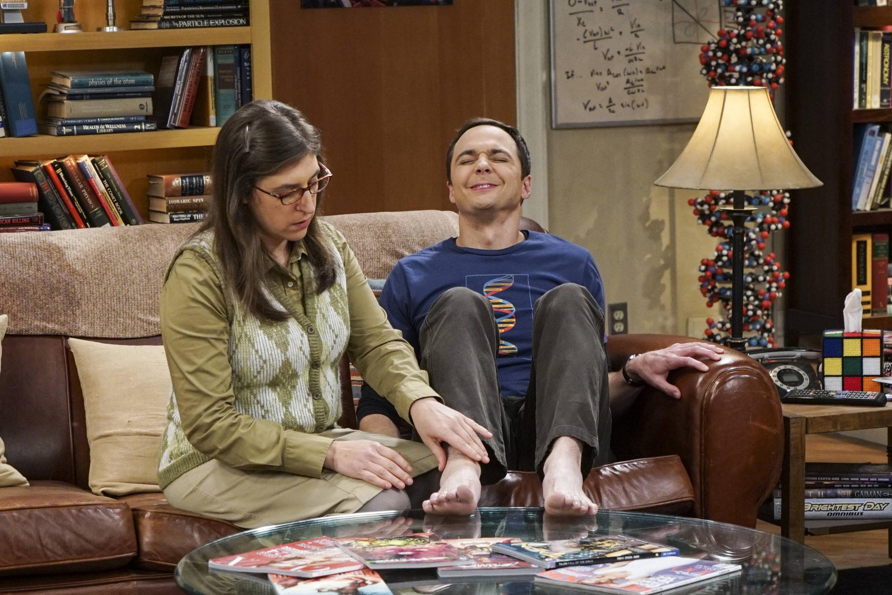 Amy and Sheldon from The Big Bang Theory sitting on a couch, Sheldon in a relaxed pose with a smile