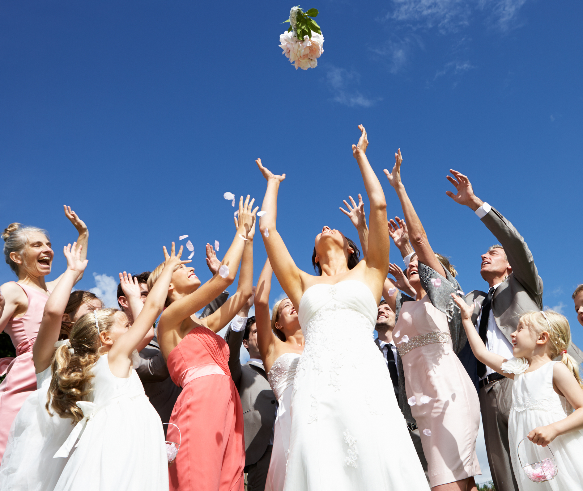 Bride and guests reaching for a thrown bouquet under a clear sky