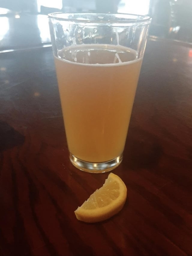A glass of beer with an orange wedge on a wooden bar surface
