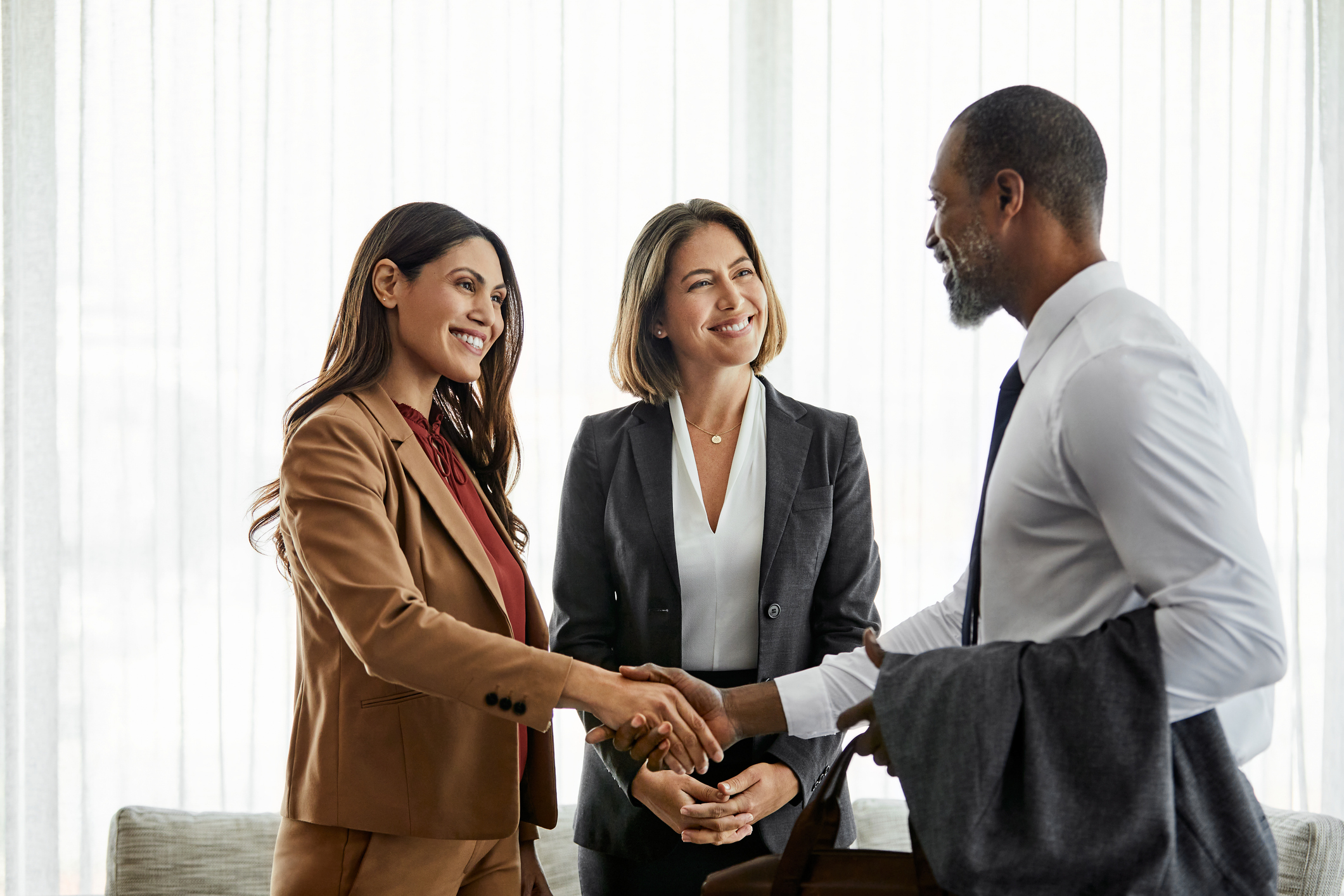 Three professionals shaking hands and smiling in a business setting