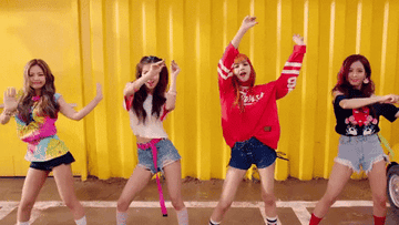 Cuatro integrantes de un grupo de K-pop bailando en un video musical