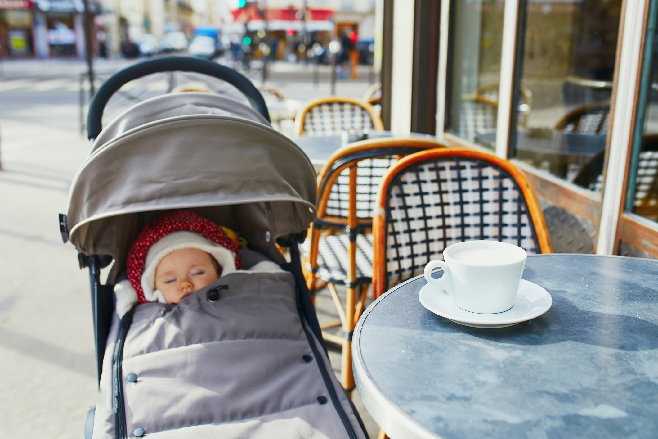 Baby in a stroller next to a coffee cup on a café table on a city street