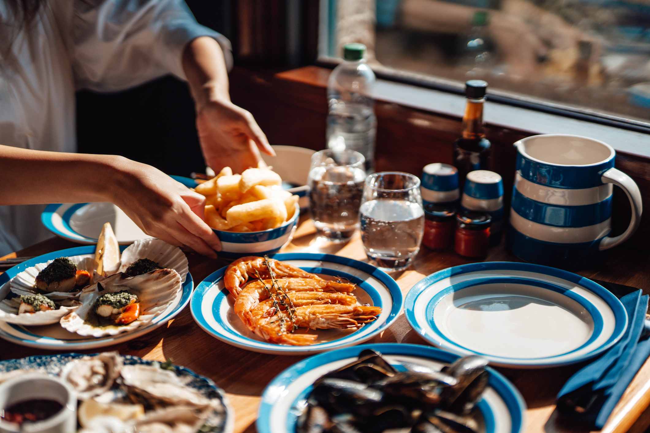 Person dining by window, seafood platter with prawns, person reaching for fries