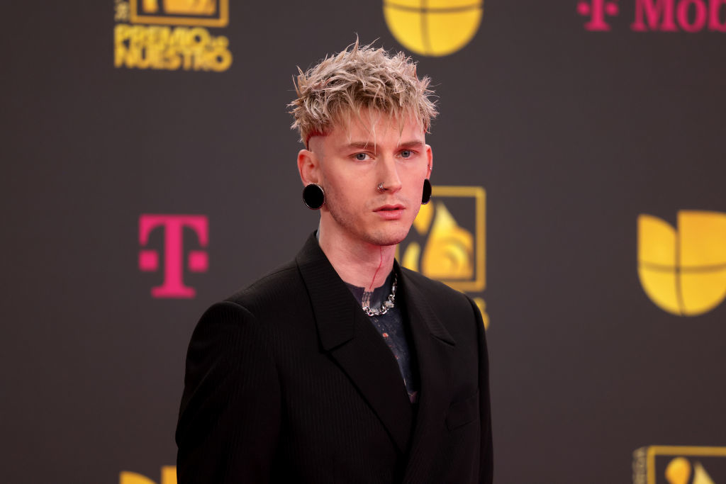 Machine Gun Kelly wearing a dark suit with spiky hair and a choker at an awards event