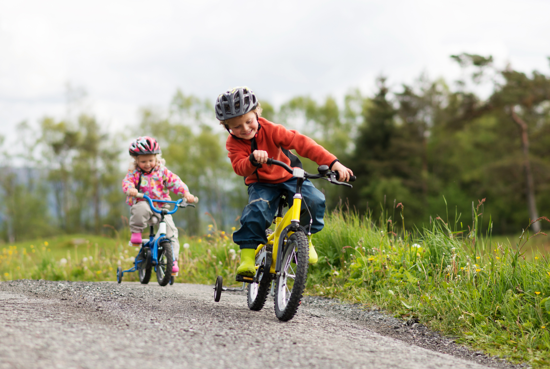 Two children biking on a gravel path with grass and trees in the background