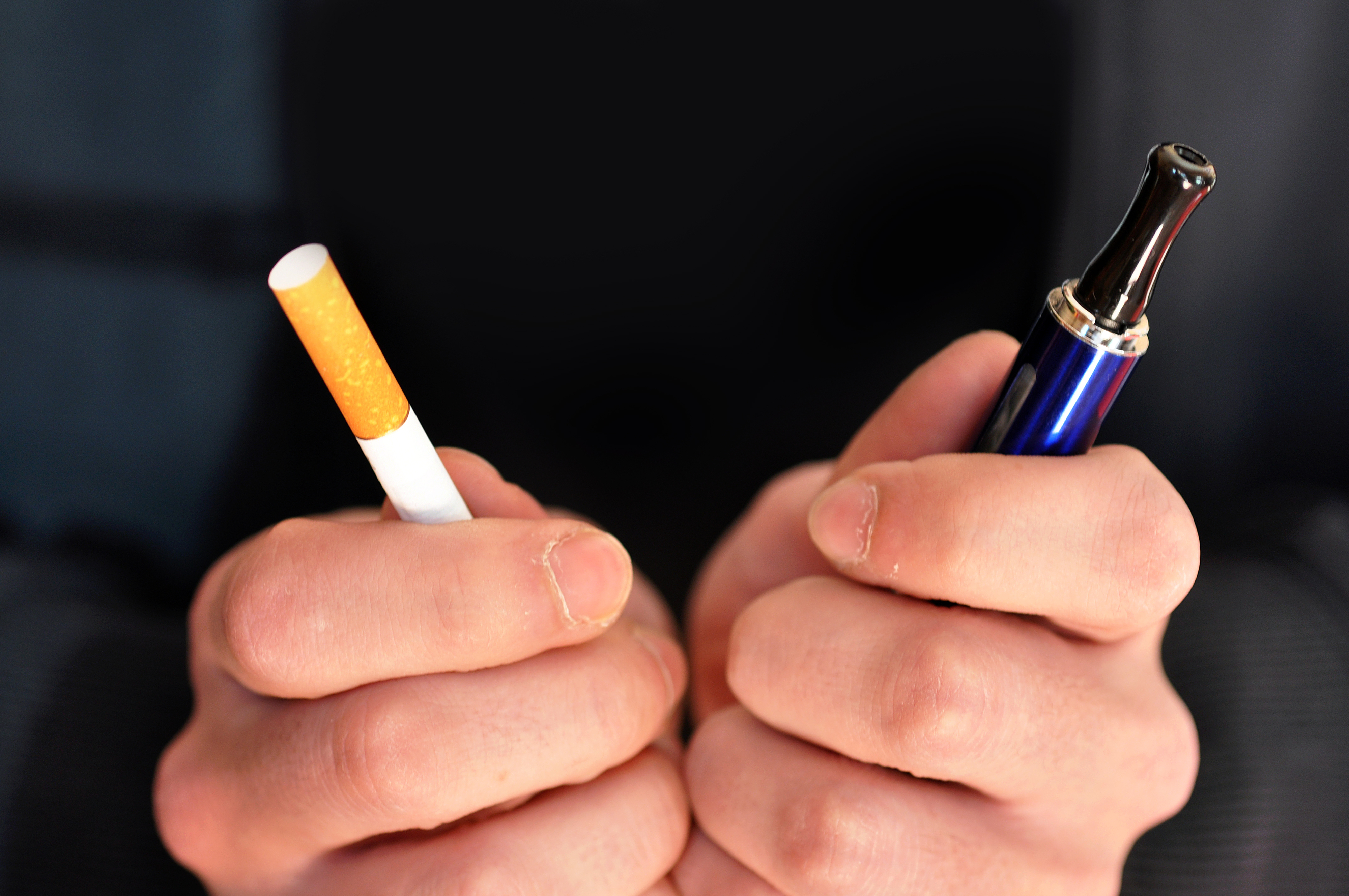 Hands holding traditional cigarette and electronic vape pen for comparison