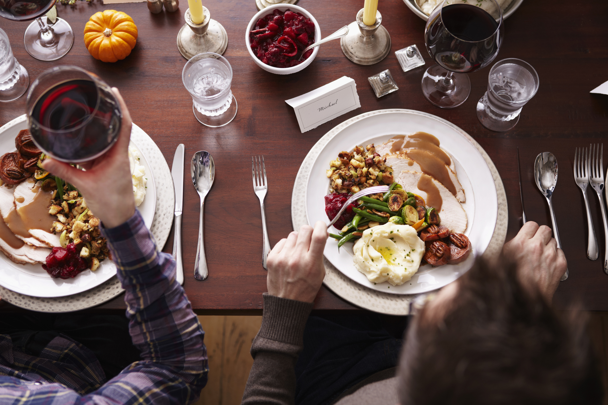 Top-down view of a person at a dining table holding a wine glass over a plate with a variety of Thanksgiving foods
