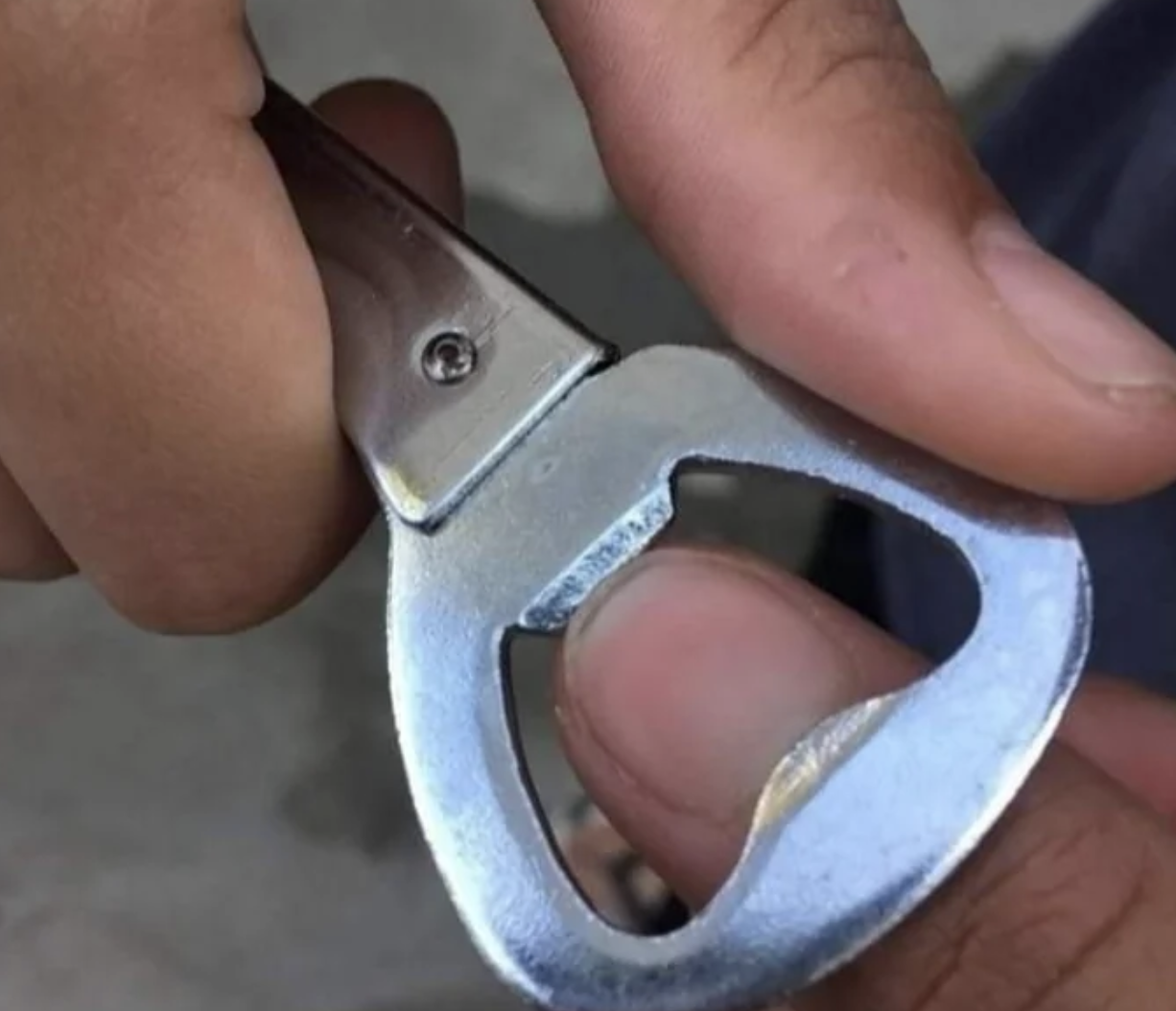 A close-up of a hand using a metallic bottle opener to open a bottle cap