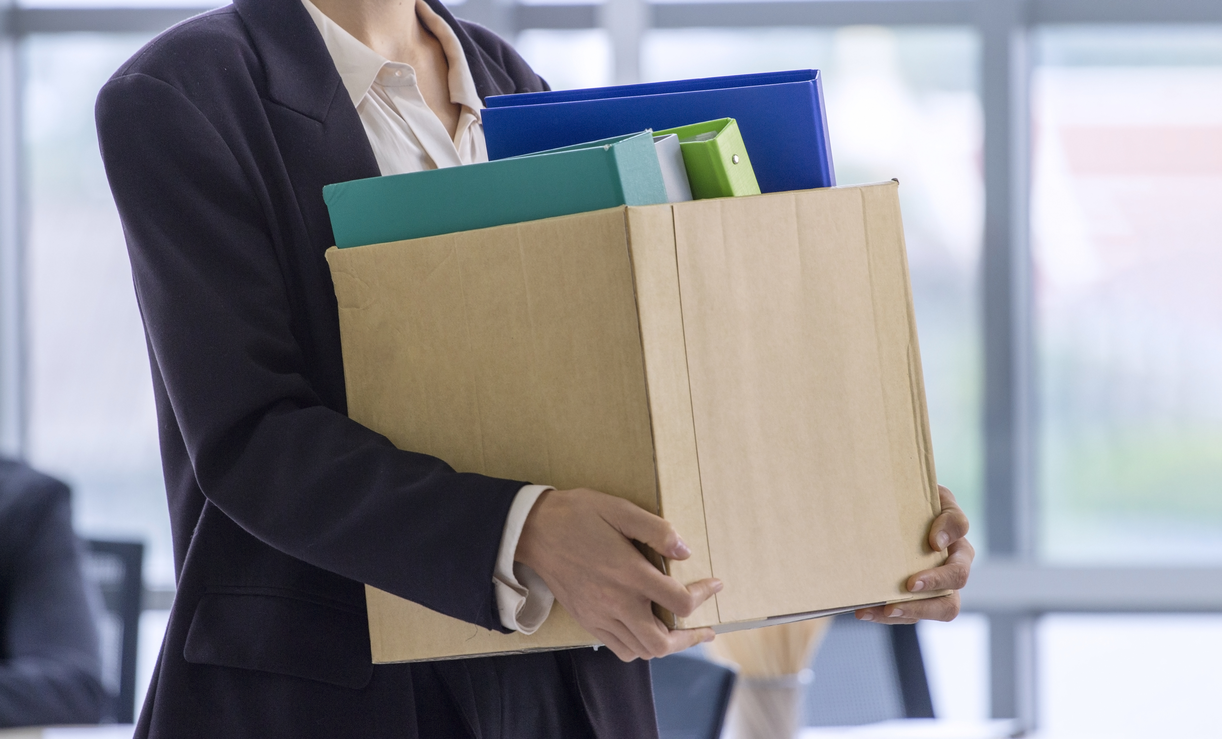 Person in a suit holding a box of work items, possibly after a job termination or relocation