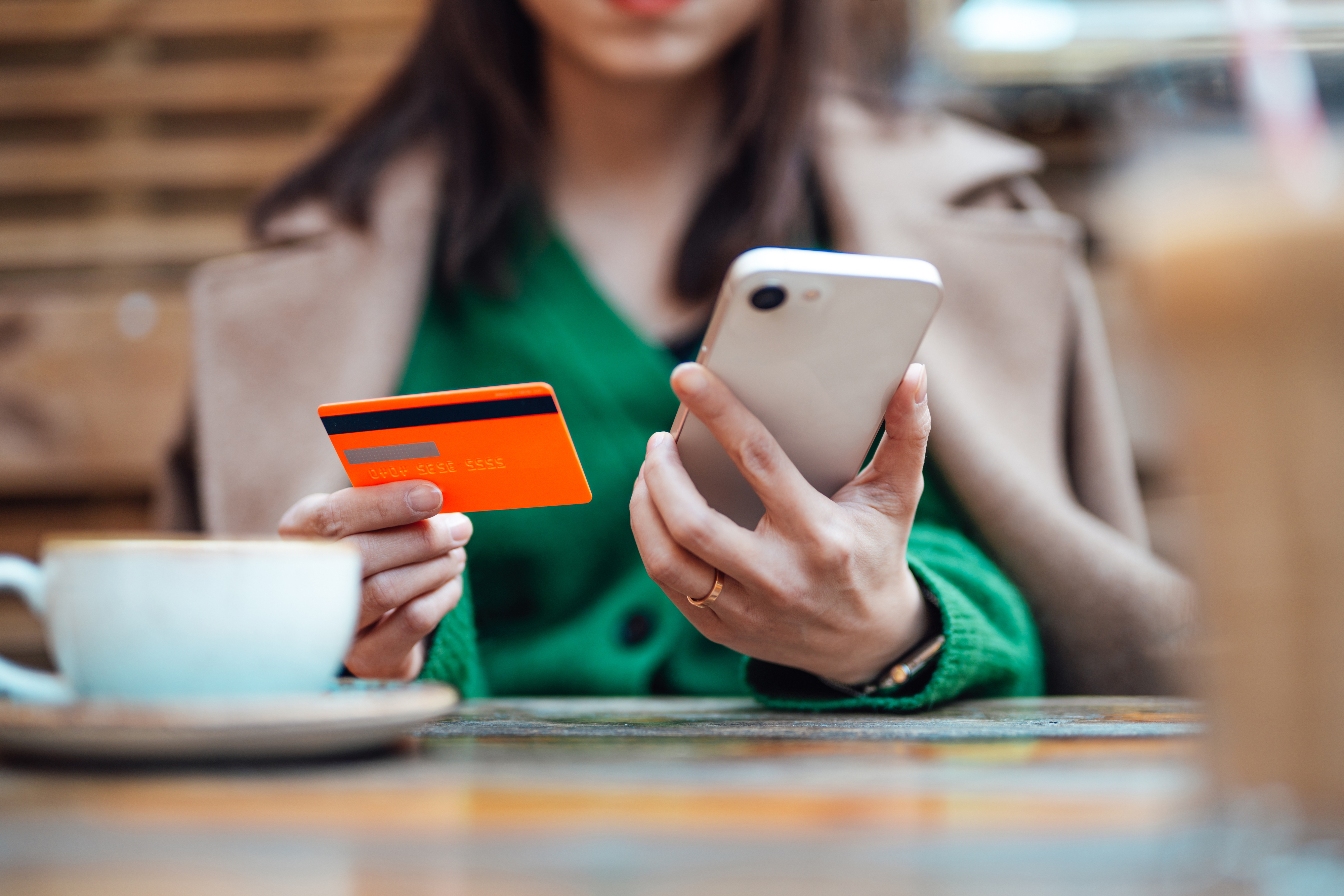Person at a table with a phone and credit card, likely managing finances or shopping online