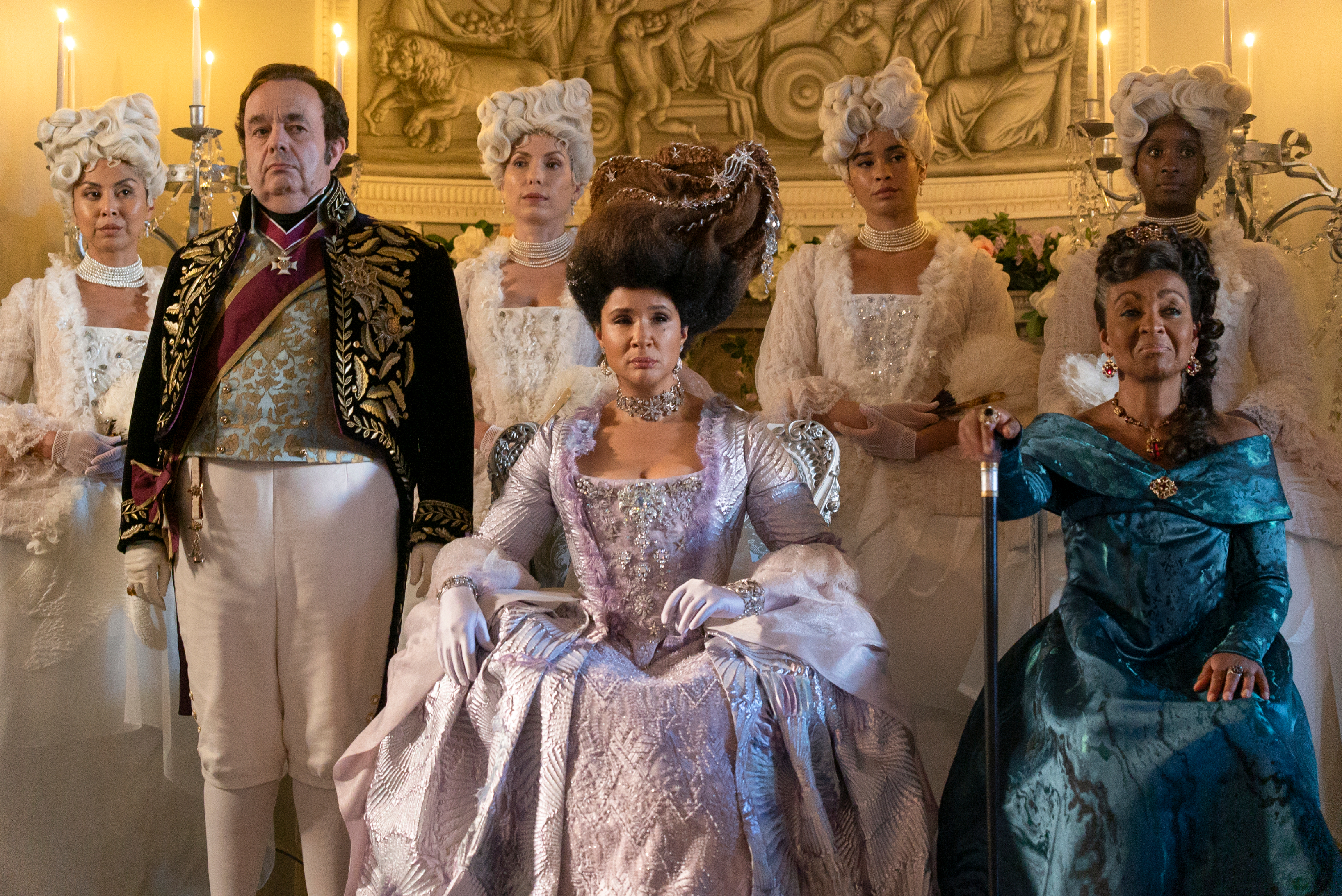 Cast in period costumes from a TV show, including characters in regal attire with elaborate hairstyles