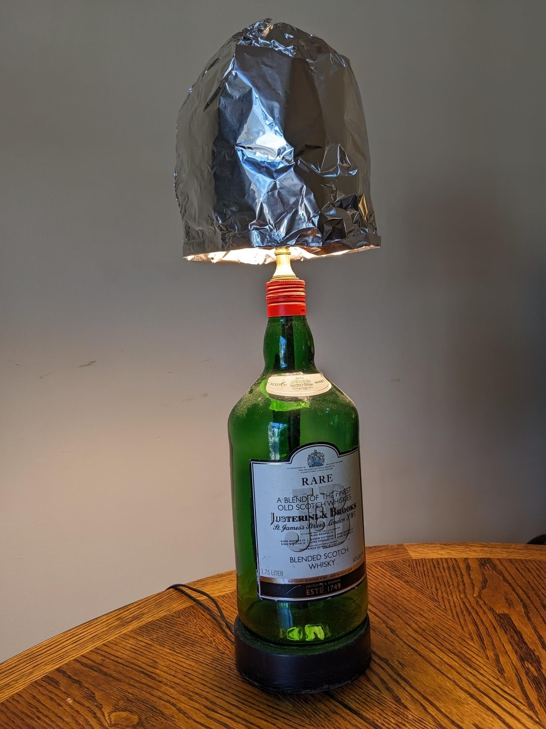 Lamp made from a green glass bottle with a silver foil shade, on a wooden table