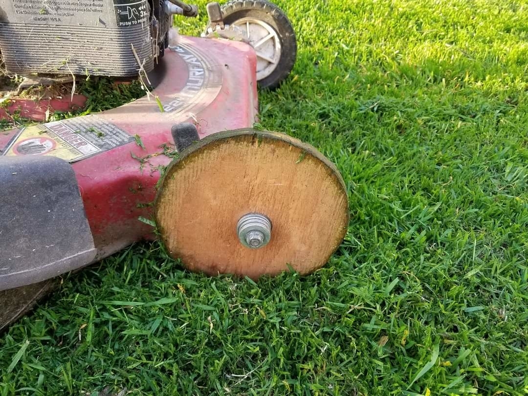 Lawn mower with a wooden wheel replacing the broken original one