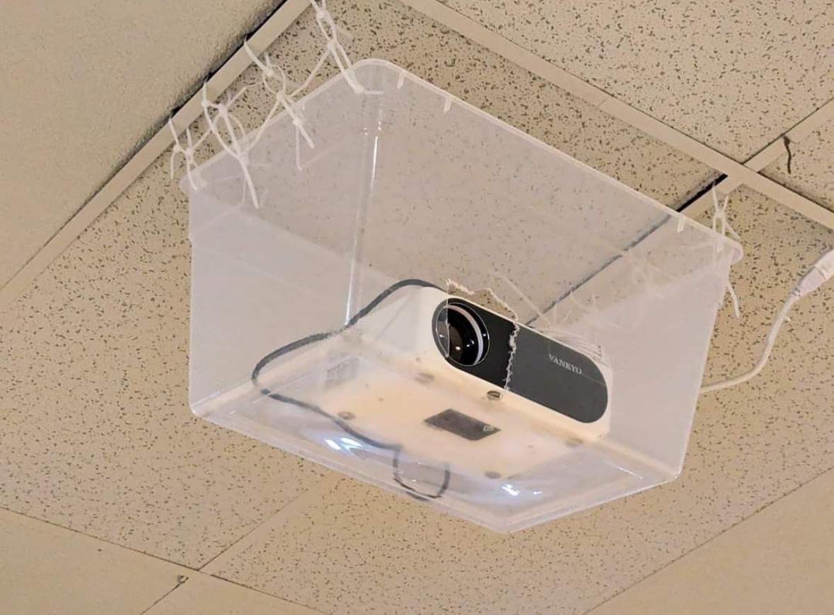 A projector in a plastic bin affixed to the ceiling