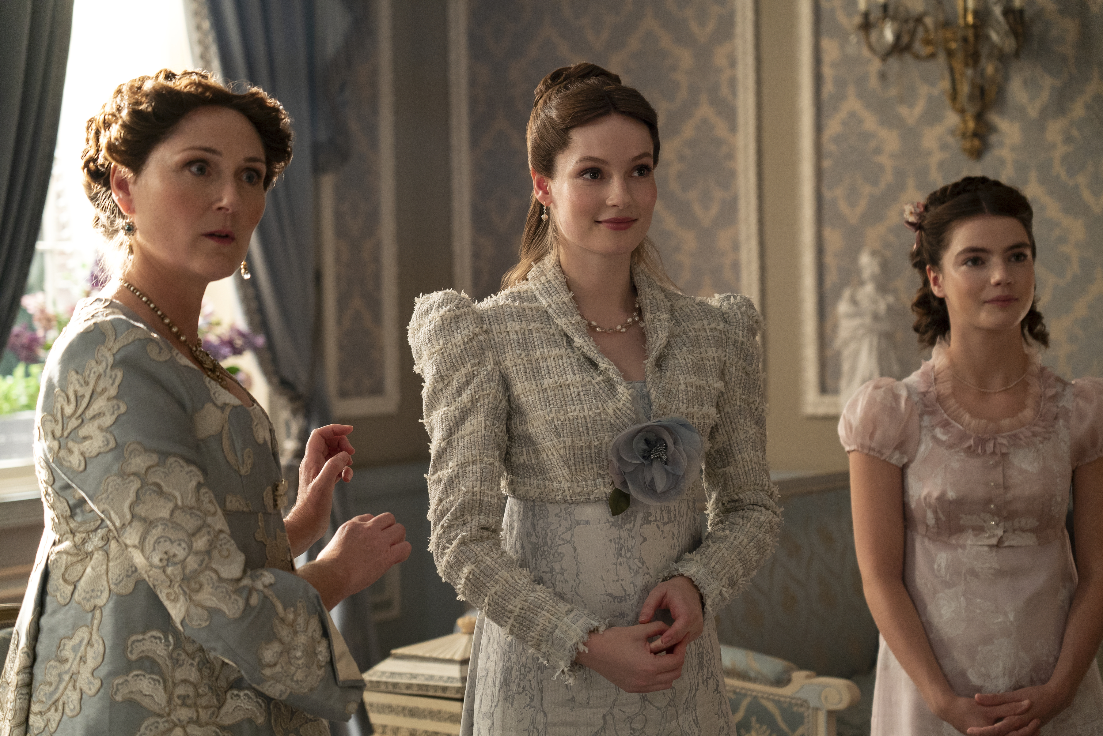 Three actresses in period costumes on a set that resembles an elegant, vintage room, likely from a historical drama