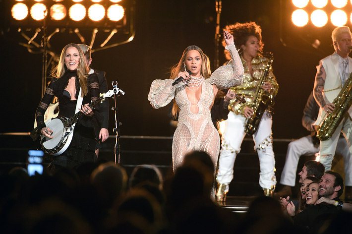 Beyoncé performing on stage in a sparkling bodysuit with musicians, including a guitarist