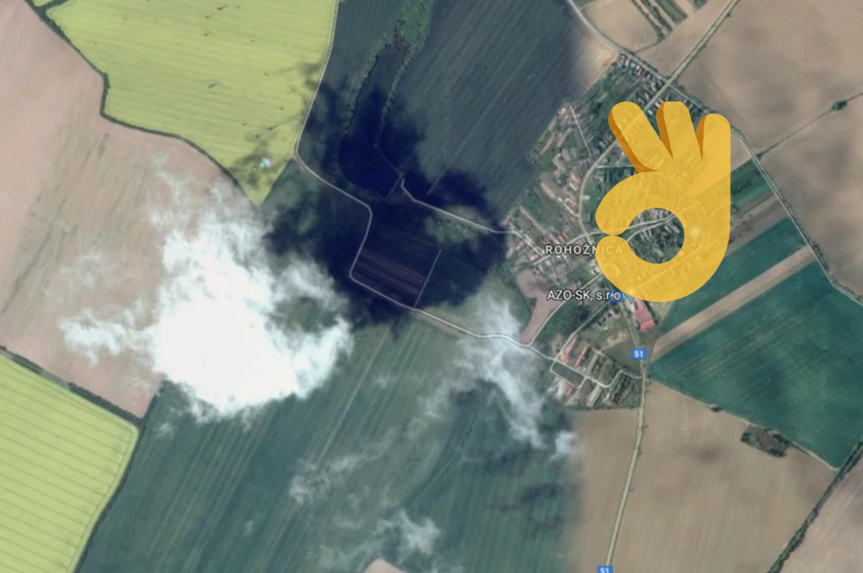 Aerial view of a landscape with smoke, overlaid by a graphic of a yellow hand making an "OK" sign
