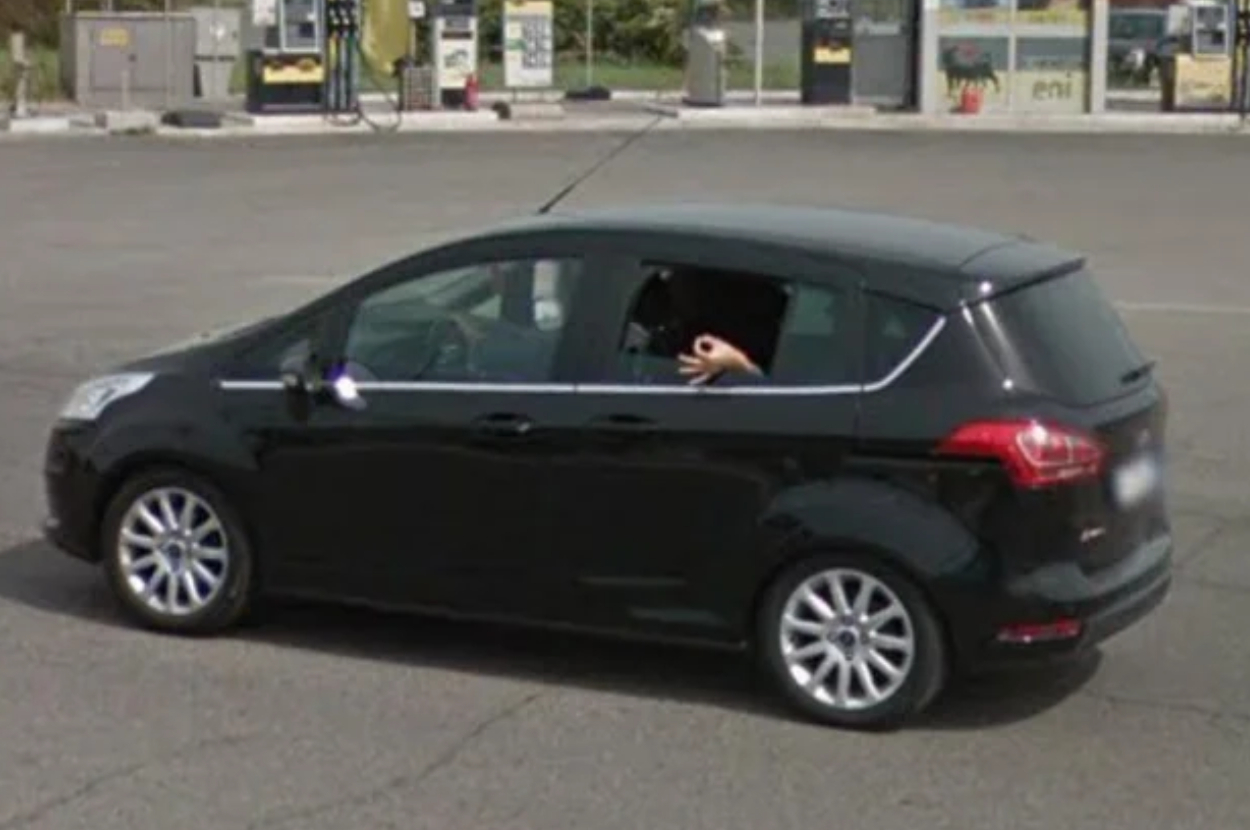 Person wearing a panda mask in the backseat of a moving black car