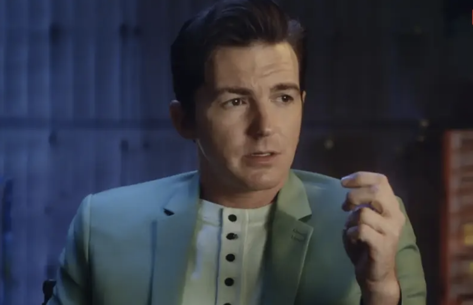 Drake Bell in a suit speaks during the docuseries