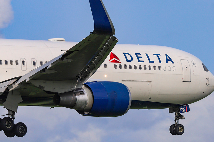 Delta Airlines aircraft mid-flight with landing gear down against a blue sky