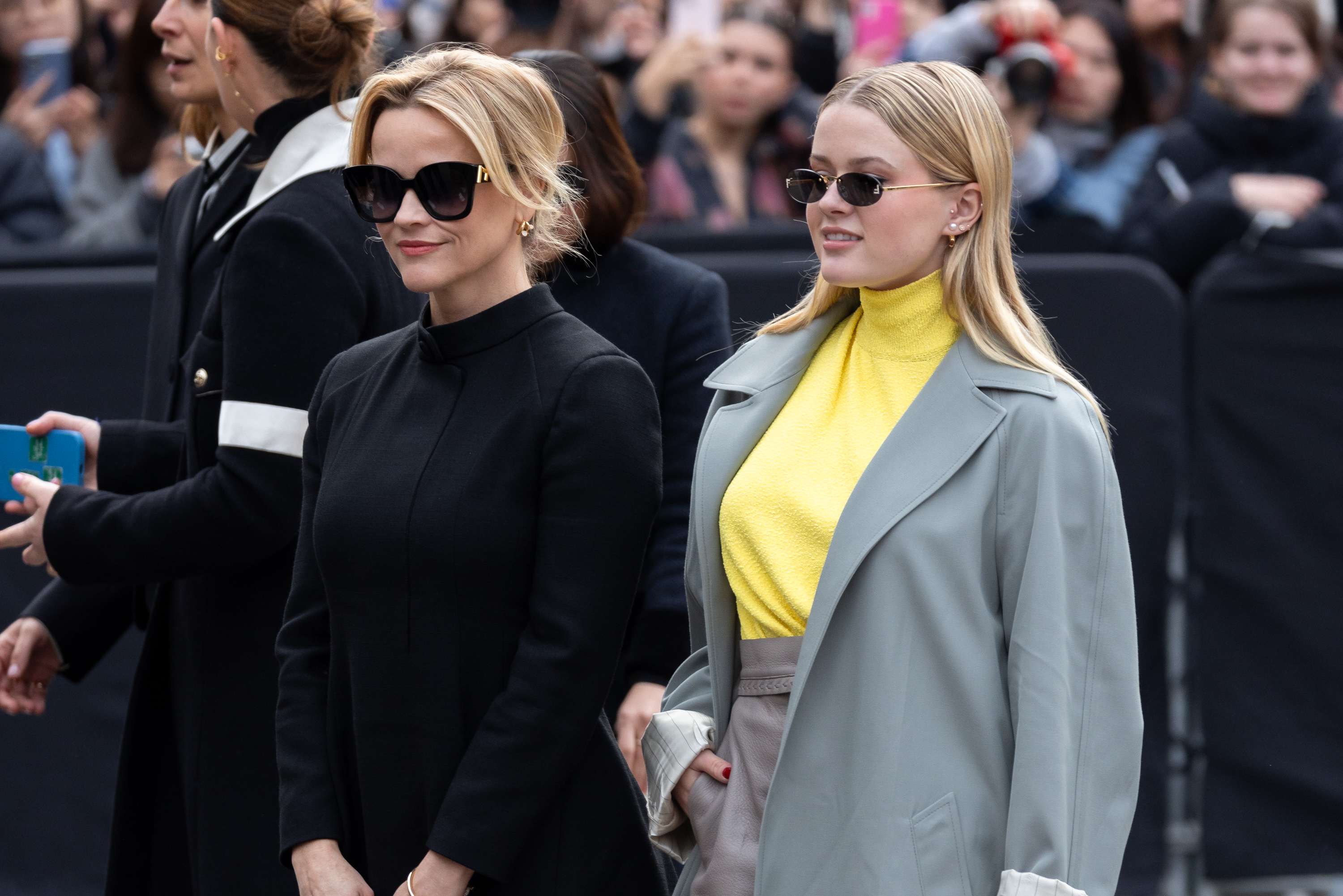 Reese in a black outfit with sunglasses and Ava in a gray coat over a yellow top