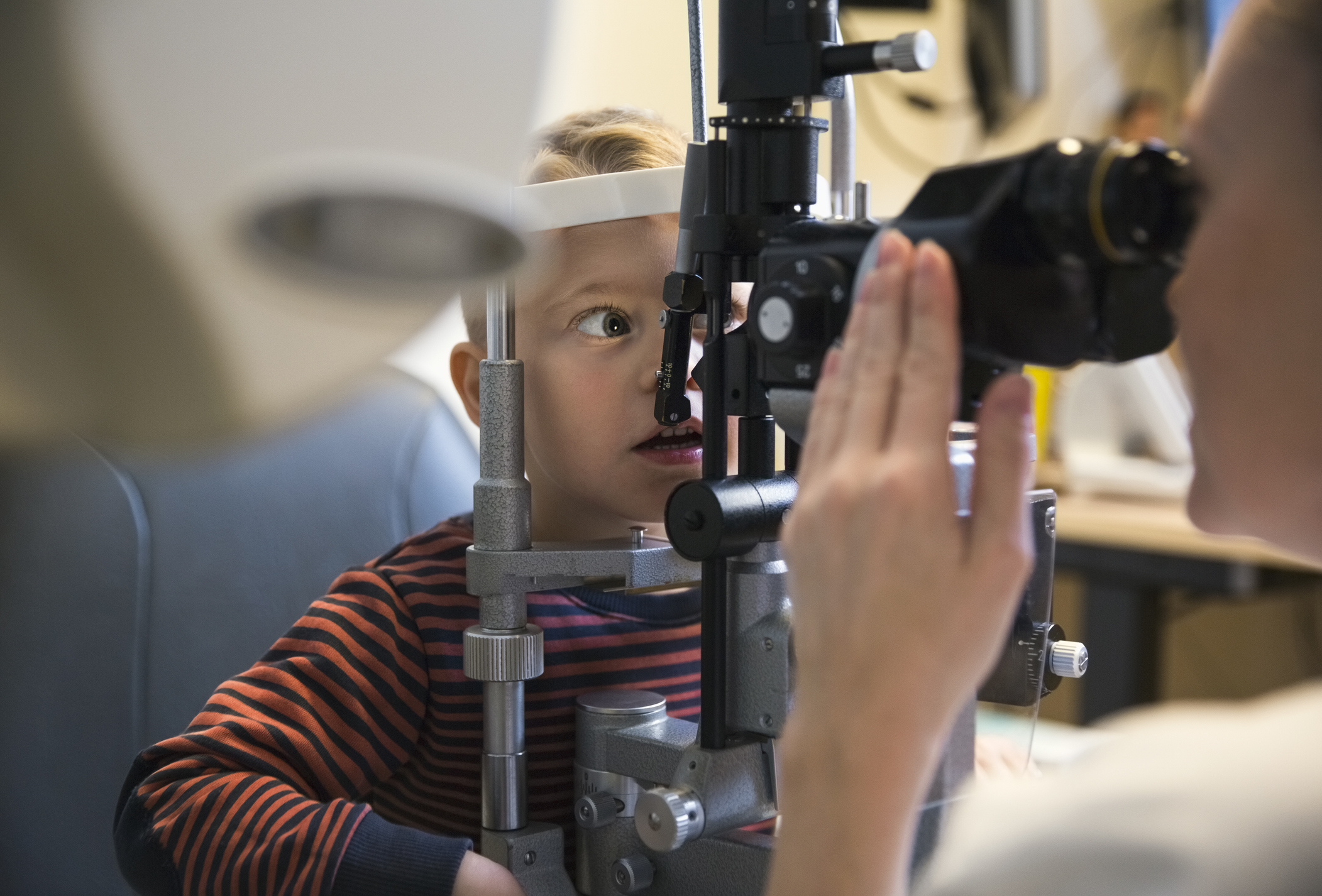 Child engaging with a vision-testing machine under an optometrist&#x27;s guidance