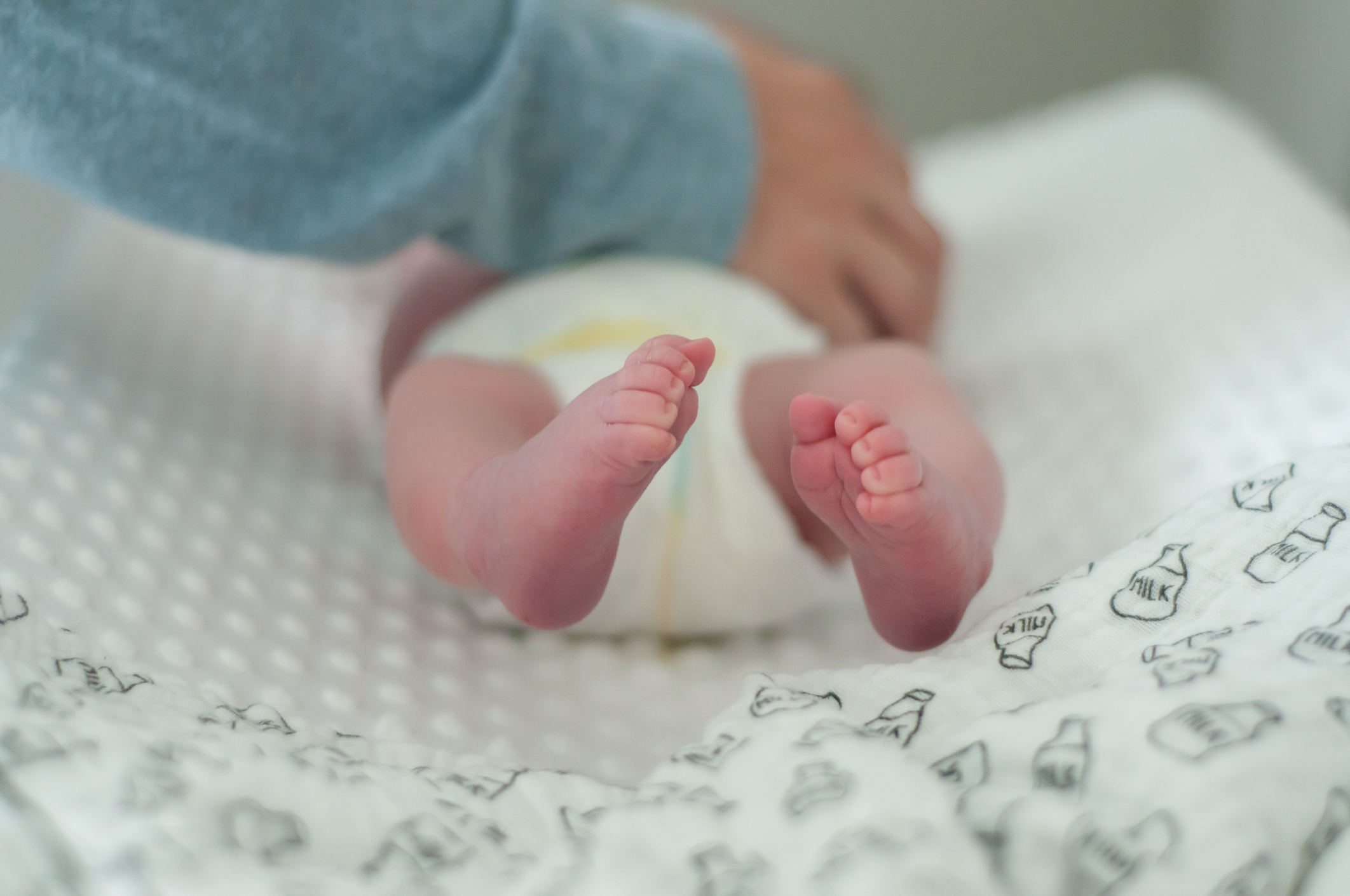 Adult&#x27;s hands gently holding a baby&#x27;s bare feet, with baby lying on a patterned surface