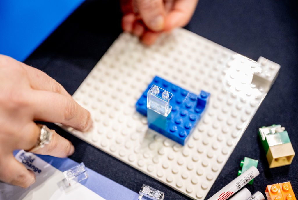 Hands assembling clear and blue blocks on a LEGO baseplate