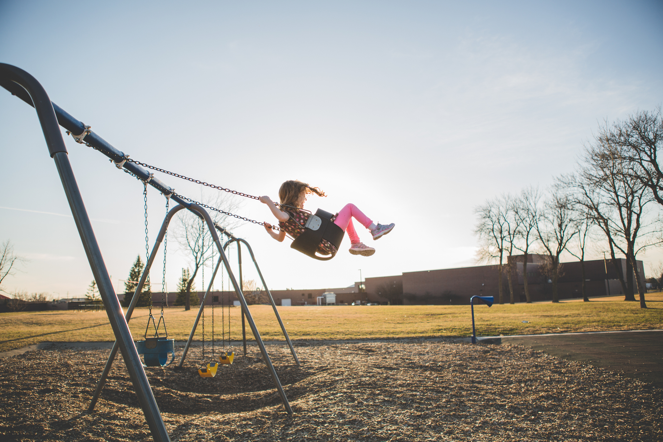 Child swinging on a playground swing set with clear skies in the background